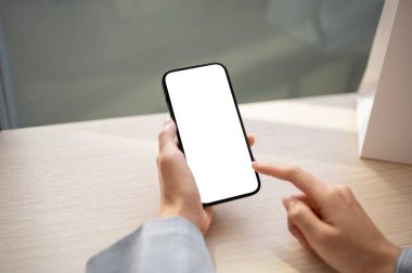 Kapalı bir masada akıllı telefonunu kullanan bir kadının yakın plan görüntüsü. Beyaz ekran akıllı telefon maketi. İnsanlar ve kablosuz teknoloji kavramları