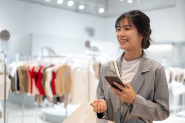 Alışveriş poşetleriyle şık giyinmiş çekici bir Asyalı kadın alışveriş merkezinde alışverişin tadını çıkarıyor. Tüketim, güzellik ve moda, yaşam tarzı, çevrimdışı alışveriş