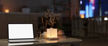 Geceleri ev çalışma alanı, beyaz ekran dizüstü bilgisayar modeli, masa lambası ve modern karanlık bir oturma odasındaki sehpanın üzerindeki aksesuarlar. 3d görüntüleme, 3d illüstrasyon