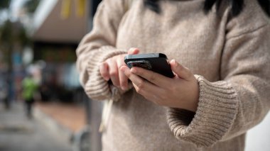 Şehirdeki caddede ya da patikada akıllı telefonunu kullanan, mesajları kontrol eden ya da haritayı kullanan Asyalı bir kadının görüntüsü. İnsanlar ve teknoloji kavramları