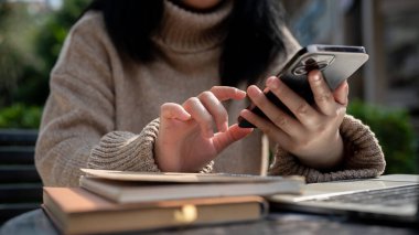 Bir Asyalı kadının akıllı telefonunu kullanarak bahçedeki bir masada uzaktan çalışırken, sohbet ederken ya da çevrimiçi blog okurken çekilmiş görüntüsü. İnsanlar ve teknoloji kavramları