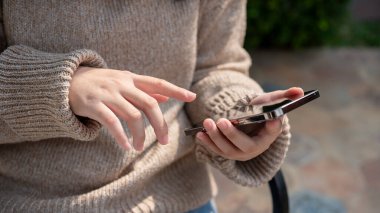 Şehir parkındaki bir bankta otururken akıllı telefonunu kullanan, sohbet eden, mobil uygulama kullanan ya da mesajlara cevap veren bir kadının yakın plan görüntüsü. İnsanlar ve kablosuz teknoloji kavramları