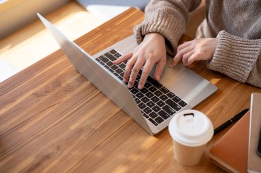 Rahat örülü bir kazak giyen bir kadın bir kahve dükkanında dizüstü bilgisayarında çalışıyor. insanlar ve yaşam tarzı kavramları