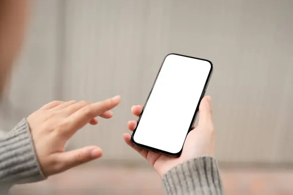 A close-up image of a white-screen smartphone mockup in a woman\'s hand with a blurred background. A woman using her smartphone outdoors. people and wireless technology concepts