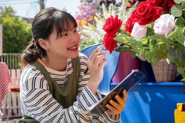 A charming young Asian female flower shop employee is checking fresh flowers stock in her shop. small business concept