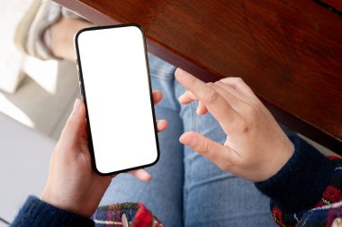Kapalı bir masada otururken akıllı telefonunu kullanan bir kadının yakın plan fotoğrafı. Beyaz ekran akıllı telefon maketi. insanlar ve teknoloji kavramları