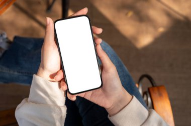 Yakın plan çekimde beyaz ekran akıllı telefon bir kadının elinde telefonuyla bir bankta otururken görüntülenir. İnsanlar ve modern teknoloji kavramları