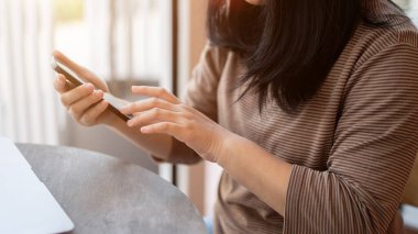 Akıllı telefonunu kullanan Asyalı bir kadının yakın plan bir görüntüsü. Bir kafede birlikte çalışırken mesajlara cevap veriyor..