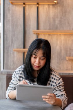 Mutlu bir Asyalı kadın dijital tabletini kullanıyor, şehirdeki bir kafede çalışıyor. Yaşam tarzı ve kablosuz teknoloji kavramları.