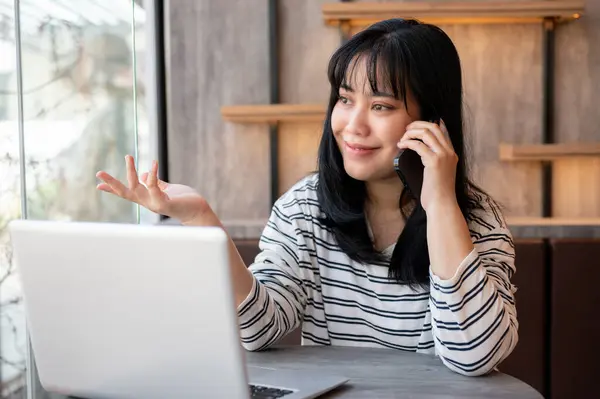 A positive, happy Asian woman is on the phone while working remotely at a cafe. people lifestyle and wireless technology concepts