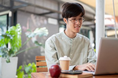 Asyalı bir adam, şehirdeki bir kafede uzaktan çalışan dizüstü bilgisayarına odaklanıyor. insanlar ve şehir hayatı kavramları