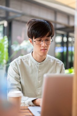 Asyalı bir adam, şehirdeki bir kafede uzaktan çalışan dizüstü bilgisayarına odaklanıyor. insanlar ve şehir hayatı kavramları