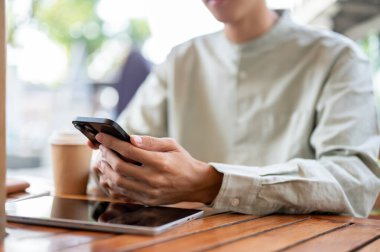 Kafedeki bir masada akıllı telefonunu kullanan bir adamın yakın plan bir fotoğrafı. Sosyal medya, mesajlar gönderme, e-postaları kontrol etme, alışveriş uygulamasını kaydırma