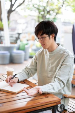 Mutlu bir Asyalı adam defterine yazmaya odaklanır, fikirleri not eder, ya da şehirdeki bir kafede otururken günlük tutar..