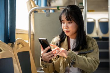 Güzel, genç, Asyalı bir bayan yolcu şehir otobüsüyle seyahat ederken telefonunu kullanıyor. insanlar ve toplu taşıma kavramları