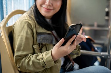 Gülümseyen Asyalı bir bayan yolcu otobüste otururken akıllı telefonunu kullanıyor, bir halk otobüsü ile seyahat ediyor. toplu taşıma ve şehir hayatı kavramları