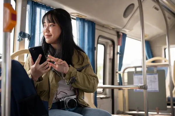 A happy Asian female solo traveler is checking a map on her smartphone while on the bus. public transportation concept