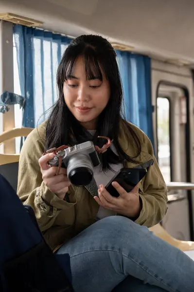 A happy Asian female solo traveler is checking pictures on her camera while on the bus, traveling to somewhere. public transportation concept