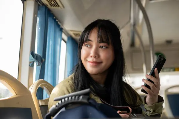 A happy Asian woman is on the bus, looking out the window, admiring the view along the street. people and public transportation concepts