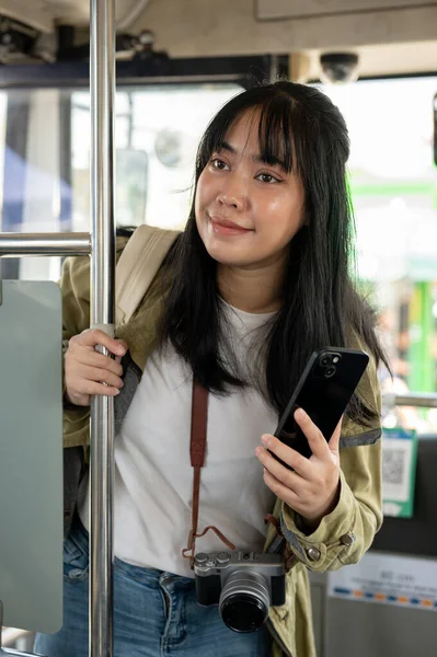 A happy Asian female traveler or backpacker is getting on a public bus, traveling by a public transportation. travel, passenger, vacation