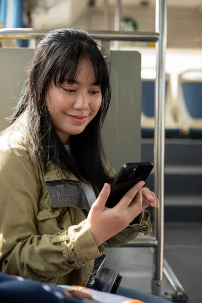 A happy Asian female traveler or backpacker is checking a map on her phone while on a public bus, traveling by a public transportation.