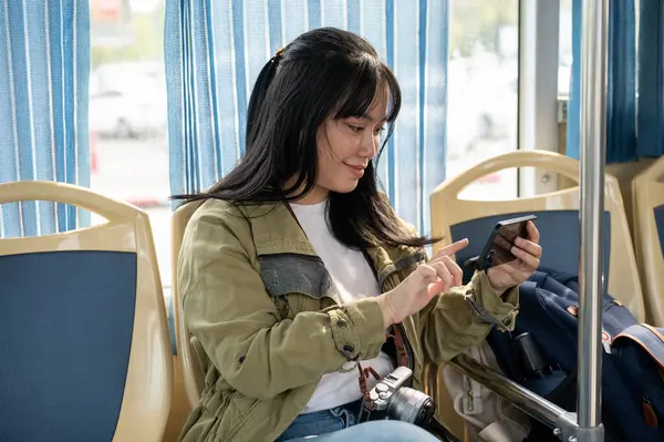 Mutlu bir Asyalı kadın otobüste akıllı telefonuyla video izlemekten zevk alıyor. modern şehir hayatı konsepti