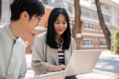 Dost canlısı, güzel bir Asyalı kız üniversite öğrencisi, üniversitenin parkında arkadaşına matematik ödevinde yardım ediyor..