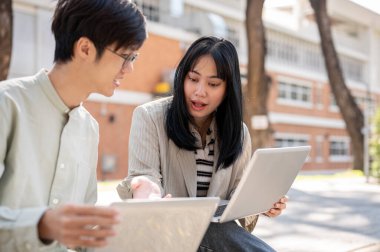 Zeki bir Asyalı kız üniversite öğrencisi üniversite parkında birlikte otururken bilgisayarında bir şeyi açıklarken arkadaşının sınav için hazırlanmasına yardım ediyor..