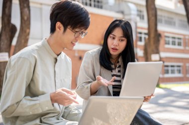Zeki bir Asyalı kız üniversite öğrencisi üniversite parkında birlikte otururken bilgisayarında bir şeyi açıklarken arkadaşının sınav için hazırlanmasına yardım ediyor..