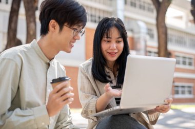 Zeki bir Asyalı kız üniversite öğrencisi üniversite parkında birlikte otururken bilgisayarında bir şeyi açıklarken arkadaşının sınav için hazırlanmasına yardım ediyor..