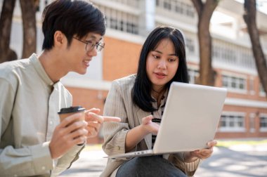 Zeki bir Asyalı kız üniversite öğrencisi üniversite parkında birlikte otururken bilgisayarında bir şeyi açıklarken arkadaşının sınav için hazırlanmasına yardım ediyor..
