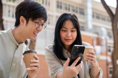 İki neşeli Asyalı arkadaş sohbet etmekten, video izlemekten ya da akıllı telefondan internet makaleleri okumaktan keyif alıyorlar..