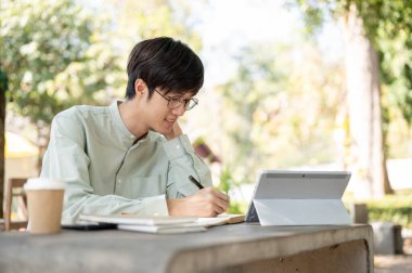 Olumlu ve zeki Asyalı bir adam bir kafede uzaktan çalışıyor, açık bir masada oturuyor, online çalışıyor, ya da ödev yapıyor..