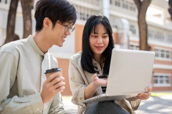 Zeki bir Asyalı kız üniversite öğrencisi üniversite parkında birlikte otururken bilgisayarında bir şeyi açıklarken arkadaşının sınav için hazırlanmasına yardım ediyor..