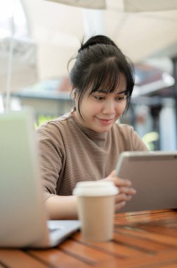 Dijital tabletini kullanan pozitif bir Asyalı kadın, şehirdeki bir kafede çalışıyor. İnsanlar ve kablosuz teknoloji kavramları