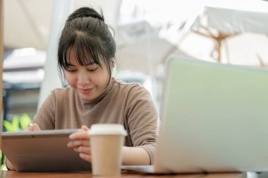 Dijital tabletini kullanan pozitif bir Asyalı kadın, şehirdeki bir kafede çalışıyor. İnsanlar ve kablosuz teknoloji kavramları