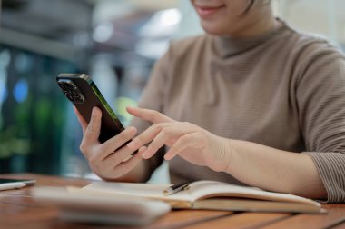 Kafedeki bir masada akıllı telefonunu kullanan, mesajlara cevap veren, sohbet eden ya da alışveriş ağında kayan bir kadının görüntüsü. İnsanlar ve kablosuz teknoloji kavramları