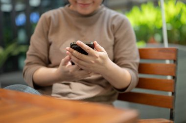 Açık hava masasında dinlenirken akıllı telefonunu kullanan bir kadının görüntüsü. çevrimiçi makaleler okumak, sohbet etmek, mesajlara cevap vermek