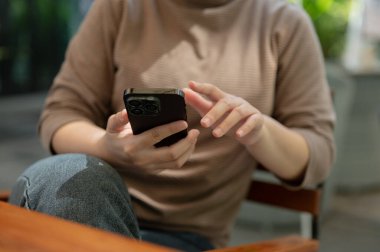 Açık hava masasında dinlenirken akıllı telefonunu kullanan bir kadının görüntüsü. çevrimiçi makaleler okumak, sohbet etmek, mesajlara cevap vermek