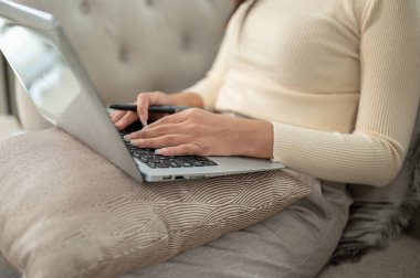 Bir iş kadınının, oturma odasındaki bir kanepede dizüstü bilgisayarına odaklanarak uzaktan çekilmiş bir fotoğrafı..