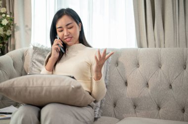 Olumlu bir Asyalı iş kadını evde uzaktan çalışıyor, dijital tabletine odaklanırken telefonla iş yapıyor..