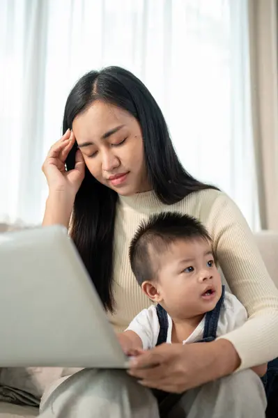 An unhappy and busy Asian mom is having a headache while working from home and taking care of her little son. mom\'s life concept