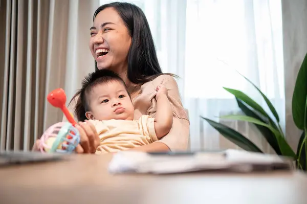 A cheerful Asian mom is laughing and enjoying playing with her baby home in the living room. family bonding, mom\'s life