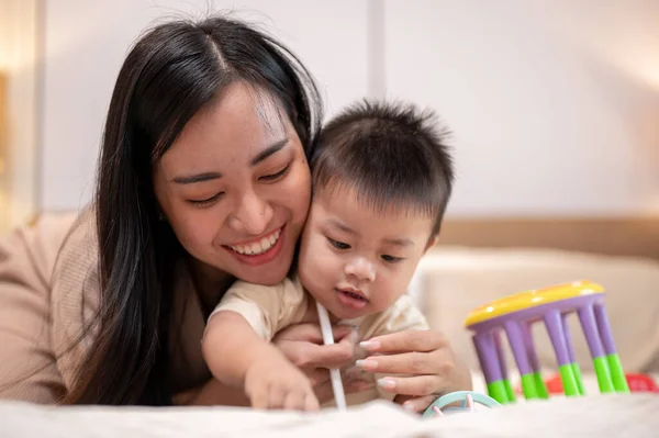 A happy Asian mom and her little son are playing and having a happy time together in bed in the bedroom. motherhood, mom\'s life, family bonding