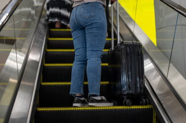 Bayan bir yolcunun bavuluyla birlikte havaalanında yürüyen merdivende çekilmiş bir fotoğrafı. seyahat, tatil, turizm