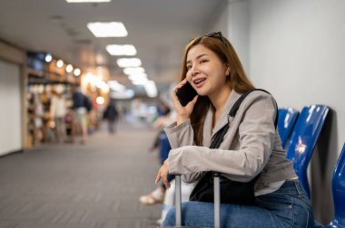 Güzel bir Asyalı bayan yolcu havaalanı terminalinde beklerken arkadaşıyla telefonda konuşuyor..