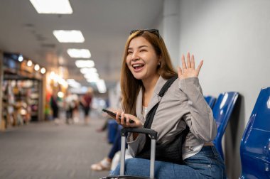 Çekici, neşeli Asyalı bir bayan yolcu arkadaşlarını karşılamak için havaalanı terminalinde beklerken elini sallıyor..