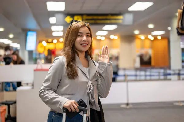 A beautiful Asian female passenger is waving her hand to say goodbye to her friends in the airport, traveling by plane.