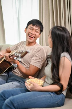 Mutlu genç Asyalı çift evde gitar çalıp şarkı söylemeyi ve birlikte romantik vakit geçirmeyi seviyor. Erkek arkadaş ve kız arkadaş, ev hayatı, eğlence.