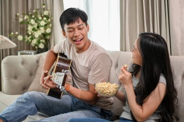 Mutlu genç Asyalı çift evde gitar çalıp şarkı söylemeyi ve birlikte romantik vakit geçirmeyi seviyor. Erkek arkadaş ve kız arkadaş, ev hayatı, eğlence.